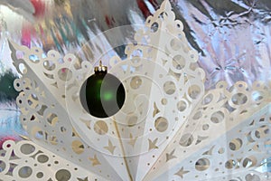 Warm and welcoming sight of paper cut-out snowflake and single green Christmas ornament hanging in window