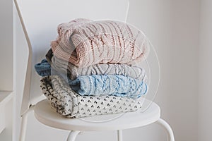 Warm woolen sweater on white chair. Knitted jumpers of white and pastel colors