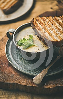 Warming celery cream soup and toast over linen tablecloth, close-up