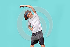 Warming up. Happy teenage boy in sportswear looking away and smiling while stretching his body before workout, standing