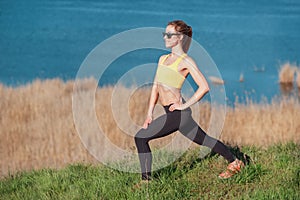 Warming up before jogging. Attractive young woman in sports clothing and sunglasses doing stretching exercises and looking concent
