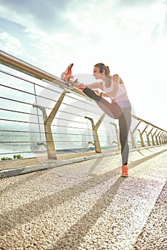 Warming up before run. Side view of disabled positive woman in sportswear and headphones stretching prosthetic leg while