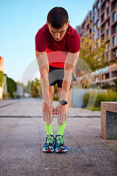 Warming-up before training. Man in sportswear standing on empty street, doing toe touching exercises before running