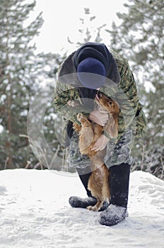 Warmly dressed man embracing loveful young russian spaniel dog in the winter forest