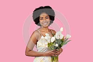 Warmly smiling young woman with natural afro hair lovingly holding a bouquet