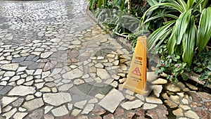 Warning Caution wet floor yellow sign on wet tiles floor at outdoor garden walkway