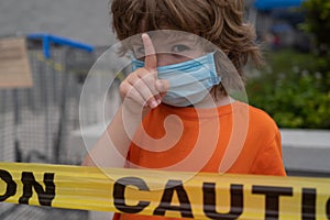 Warning. Cute child in the mask shows a warning sign during coronavirus. Young boy in quarantine. Isolation. Homework