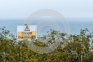 Warning of eroding cliffs.  notice to avoid getting close to the cliffs. Coastal yellow triangle danger sign