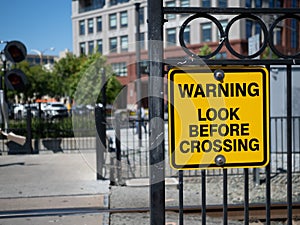 Warning look before crossing yellow warning sign at train crossing in city