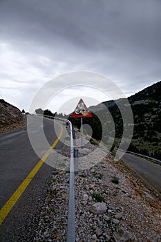 Warning road sign with bullet holes in the background of the mountain landscape of Crete