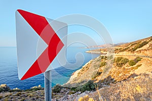 Road sign at the sharp turn of the serpentine and winding country road along the picturesque sea coast. Danger and risk of