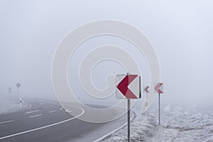 Warning road signs before dangerous curve in dense mist