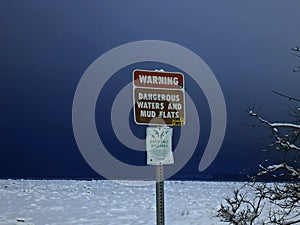 Warning Sign in Anchorage, Alaska saying Dangerous Waters and Mud Flats, Important Bird Area. Snowy field or harbor in winter