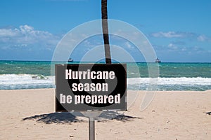 Warning sign on beach next to the trunk of a palm tree on a sunny day with a blue clear sky warning that it is hurricane season