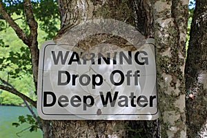A warning sign being absorbed by a tree on the shores of lake O`Law on Cape Breton Island