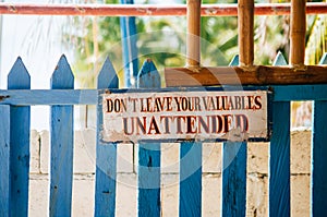 Warning sign board hanging on the wooden gate: Don`t leave you valuables Unattended