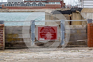 A warning sign on flood gates that reads Danger strong tides and heavy wash from passing vessels it is dangerous to swim in this
