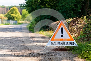 Warning sign with German text reading tree felling BaumfÃ¤llung in front of a logged tree trunk. Concept of forestry.