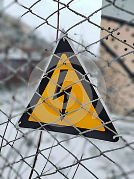 A warning sign hangs on a wire fence about high electrical voltage behind it