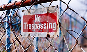 Warning sign No Trespassing mounted on a chain-link fence, with a weathered, bold red background, enforcing property boundaries