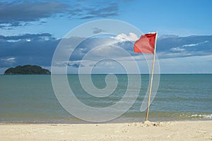 Warning sign of a red flag at a beautiful clean beach with a blue sky, cloud and the sea with small green island