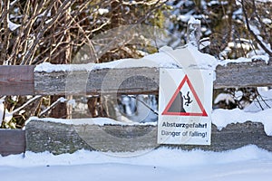 Warning sign on snow covered mountain path with text: Absturzgefahr! - Danger of falling!