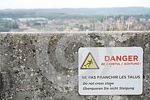 Warning sign to prevent tip over, overturn, in English, German and French language attached to the stone wall . photo