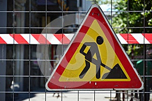 The warning sign `under construction` is attached to a metal mesh fence with a red and white striped signal tap