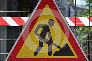 The warning sign `under construction` is attached to a metal mesh fence with a red and white striped signal tap
