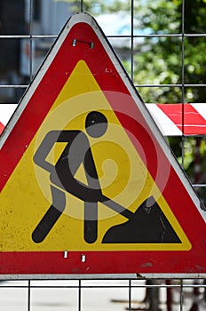 The warning sign `under construction` is attached to a metal mesh fence with a red and white striped signal tap