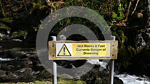 Warning sign - wet rocks and fast currents danger of drowning with waterfall and forest background