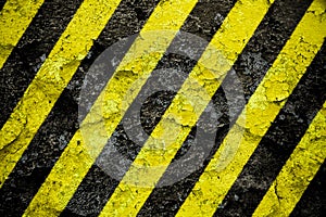 Warning sign yellow and black stripes pattern painted over concrete cement wall facade with peeling cracked paint background.