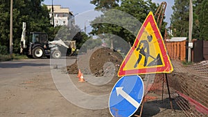 Warning signs on closed road under construction with arrow sign, hinders traffic in the city. On the background tractor