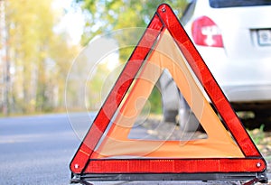 warning stop sign on the road against the background of a white car and forest. concept of roadside assistance, travel incidents,