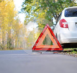 Warning stop sign on the road against the background of a white car and forest. concept of roadside assistance, travel incidents,