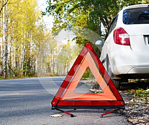 Warning stop sign on the road against the background of a white car and forest. concept of roadside assistance, travel incidents,