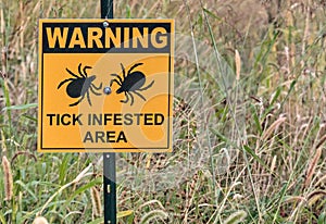 warning tick infested area sign in a grassy field, public park (lyme disease prevention) photo