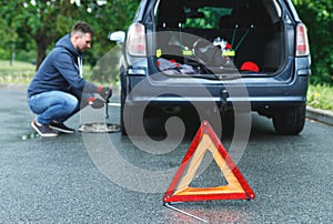 Warning triangle and man changing car wheel