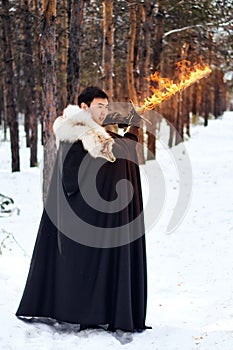 A warrior in black quilted clothes in a black cloak with a white fur collar and a long fiery sword in his hands