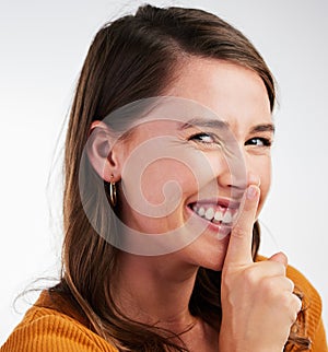 That was for your ears only. Studio shot of a young woman smiling and signalling to be quiet against a background.