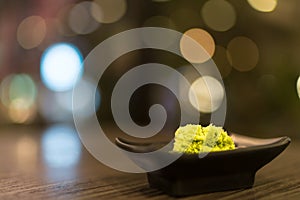 Wasabi in black saucer on wooden table with depth of field effect, Japanese food`s condiment, bokeh background