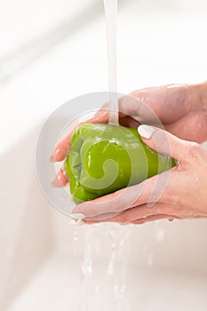 Wash before eat: female washing green pepper in water in sink before cooking salad. Hygiene concept