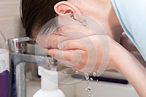 Wash a woman`s face with a spray of water, wash her face in a sink under a stream of cold water. Home facial skin care