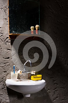 Washbasin with a glass for a toothbrush and a soap box on it under the mirror in a prison cell