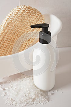 washcloth in a miniature white plastic tub and a bottle of skin care product against a gray background