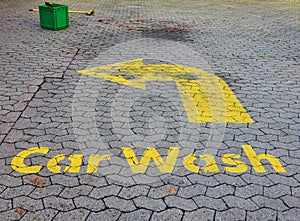 Washed-out old ugly painted yellow entry sign for a car wash on a dirty old pavement of a petrol station