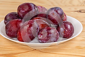 Washed plums on dish on rustic table, side view closeup