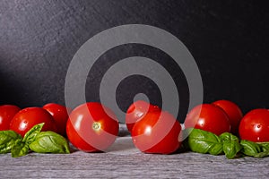 Washed ripe tomatoes and basil leaves, on black background