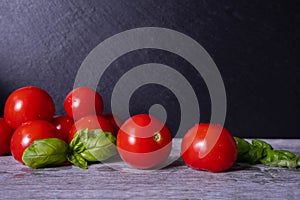 Washed ripe tomatoes and basil leaves, on black background