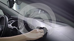 Washerman is wiping control panel of modern auto by black sponge, sitting inside, close-up of hand